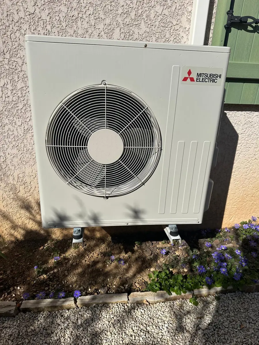 Unité extérieure Mitsubishi Electric posée sur un mur de jardin fleuri